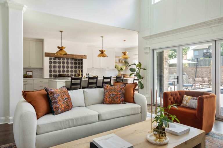 Modern living area with a beige sofa orange armchair and adjacent kitchen featuring white cabinetry remodel by AMI Build 768x512